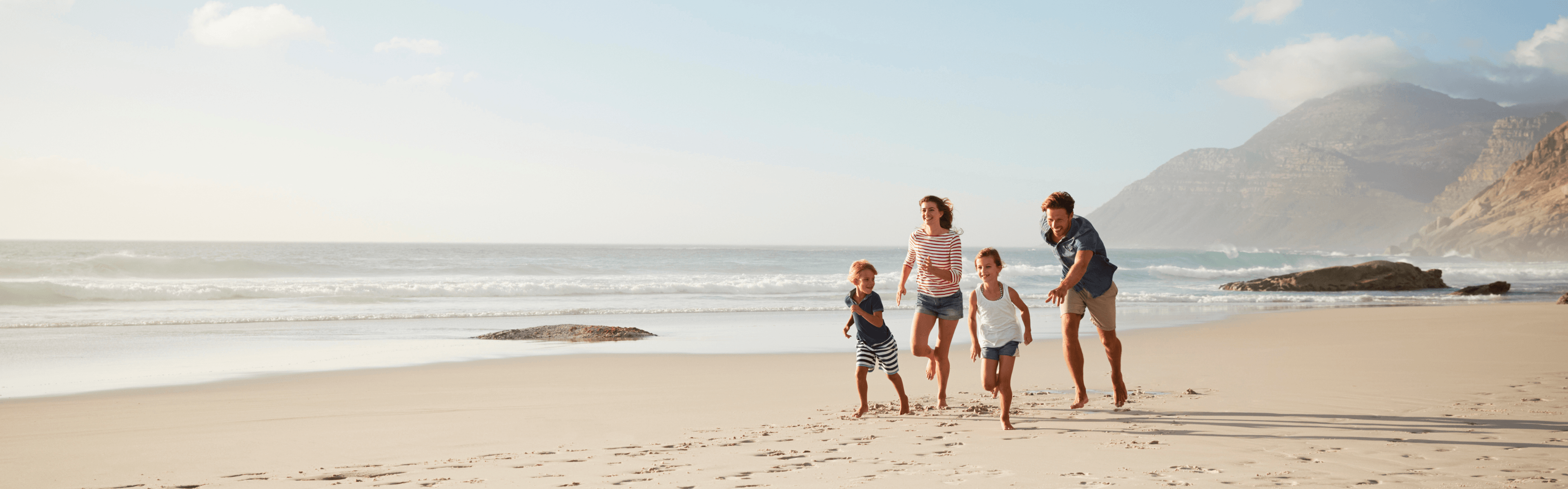 Vier Personen, eine Familie, rennt einen Strand entlang. Alle sind glücklich, das Licht ist hell.