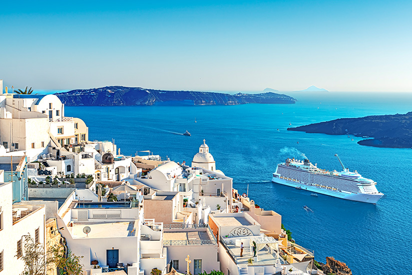 Blick auf Santorinis weiße Häuser mit Kuppeln und ein Kreuzfahrtschiff im tiefblauen Meer der Ägäis